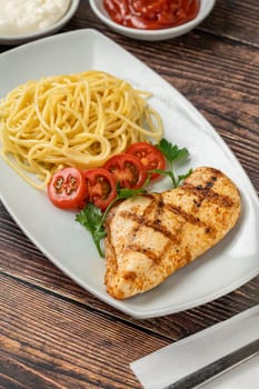 Spaghetti and grilled chicken on a white porcelain plate with buttermilk and sauces on wooden table