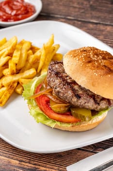 Delicious grilled homemade hamburger with beef, tomatoes, cheese, and lettuce on rustic wooden background