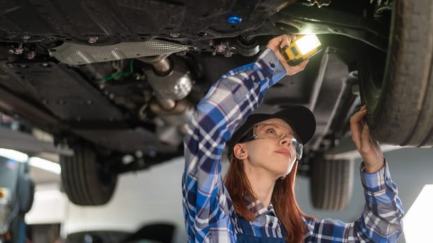 A female mechanic inspects a lifted car. A girl at a man's work