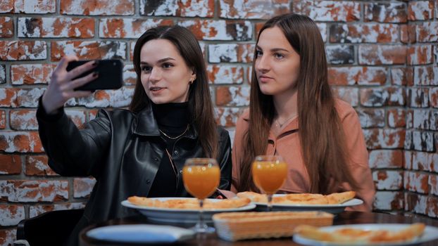 Two girls are sitting in a cafe and taking a selfie on the phone