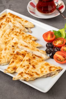 Traditional Turkish flatbread or Gozleme with tomatoes, olives and tea on dark stone table