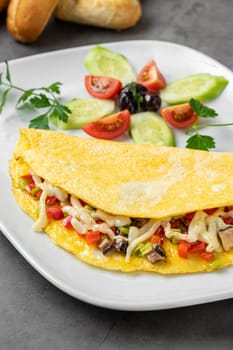 Omelet with cheese, mushrooms and vegetables on a white porcelain plate