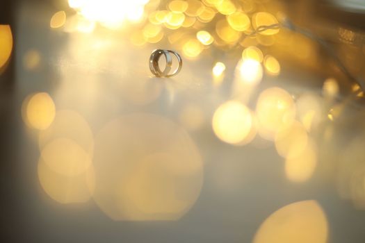 Wedding rings on blured bokeh glowing golden background. Symbol of love and romance on a textured glitter background with copy space for your greeting or congratulations.