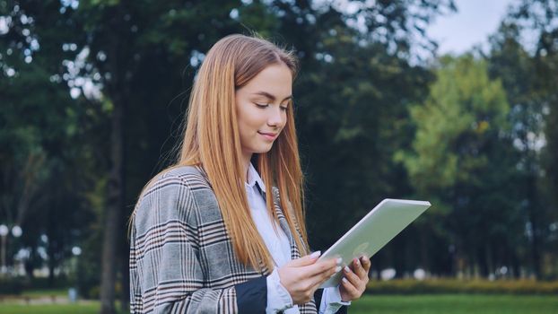 A young girl walks with a tablet in the park