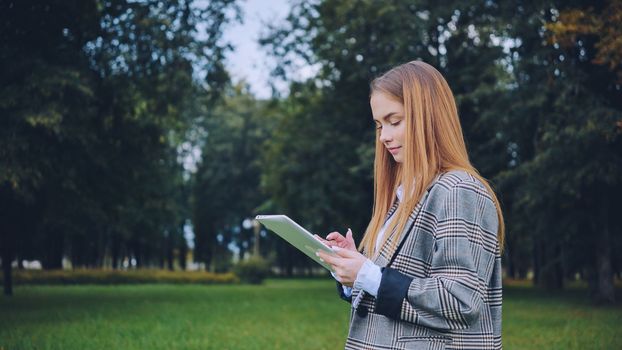 A young girl walks with a tablet in the park