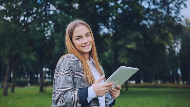 A young girl walks with a tablet in the park