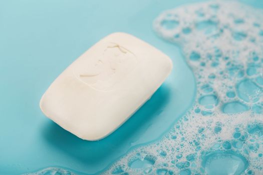 A piece of white soap with foam on blue background. Backdrop with copt space.