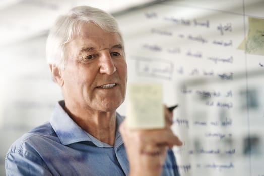 Owning a business is planning and execution. a senior businessman writing down ideas with a pen marker on a glass wall in the office