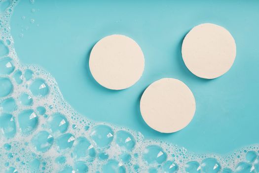 Three bars of round soap with foam on a blue background