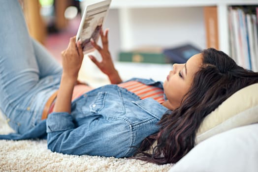 Enjoying the perks of wireless technology. a young woman using her digital tablet while lying on the sofa