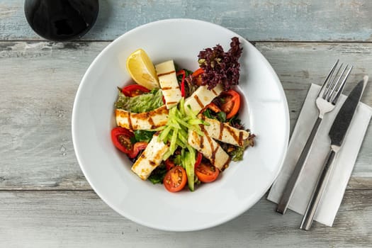 Salad with tomato and halloumi cheese on wooden table