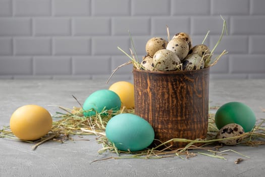 Easter composition from a clay vessel with quail eggs in hay surrounded by painted chicken eggs. Selective focus.