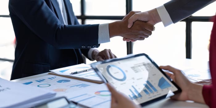 Shaking hand business leaders talk about charts, financial graphs showing results are analyzing and calculating planning strategies, business success building processes.