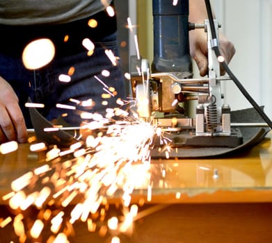 Worker man cutting a metal pipe in two pieces and lot of sparks flying straight into the camera close-up.