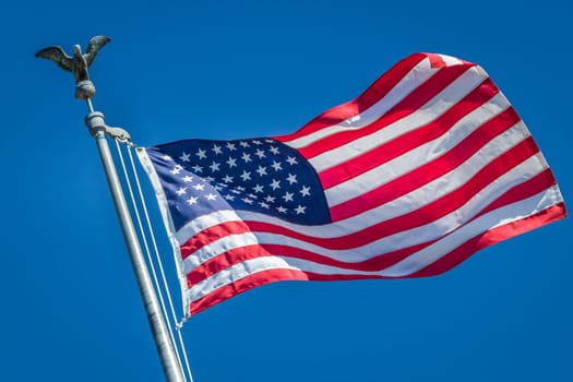 American flag waving on pole with eagle and bright vibrant red white and blue colors against blue sky