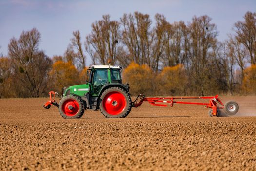 In the background, in front of a row of trees, a farmer is plowing a field with a tractor