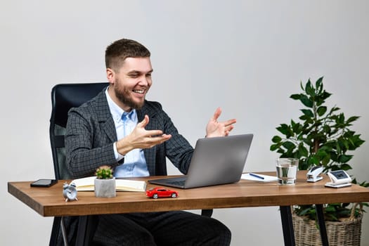 young friendly man talking on video call to client, sitting on chair at desk, using laptop pc computer
