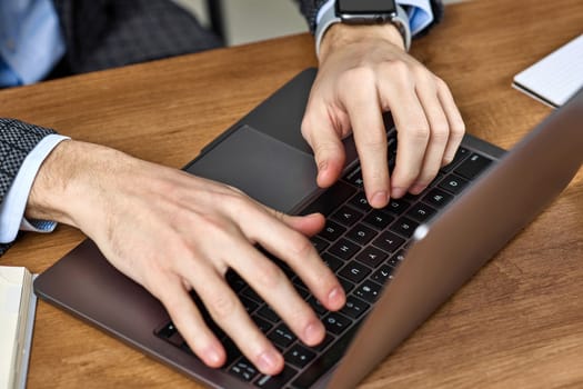 Male hands typing on a laptop keyboard on wooden desk. Close-up