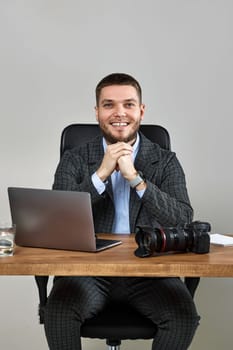 Professional male photographer smiling cheerfully while working at desk. dslr camera on table