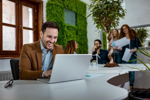 Young handsome successful smiling businessman analyzing graph plans that show success, and working on laptop in the office.