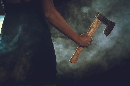 Close-up of a woman's hand with a axe in a smoky dark space. 