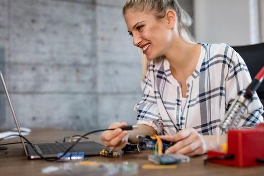 Young smiling woman technician focused on the repair of electronic equipment  and checking something on the laptop.