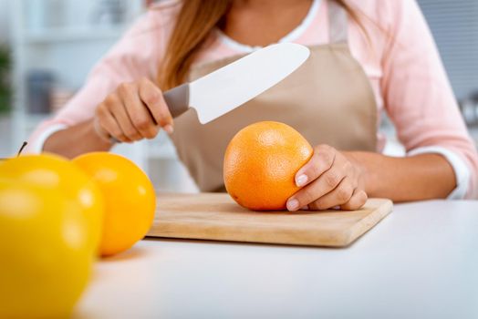 Close-up of a female hands cutting red grapefruit on the kitchen board.