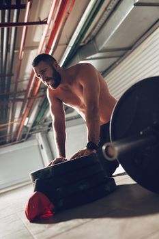 Young exhaustion muscular man resting after heavy hard training at the garage gym.