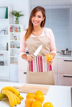 Cute young woman prepared to cut the grapefruit in kitchen. Looking at camera.
