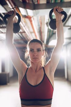 Young muscular woman exercise with kettlebells on hard training at the garage gym.