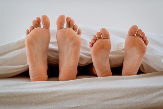 The feet of a heterosexual couple under the covers in bed.