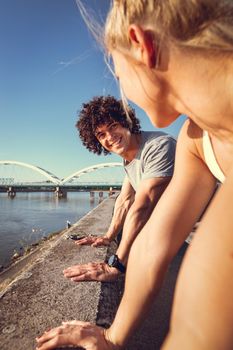 Young happy smiling couple training outdoors doing push-ups during outdoor cross training by the river.