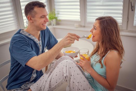 Happy, loving, couple, spending sunday morning in happiness. Man is feeding his loved woman, looking each other with smile. 