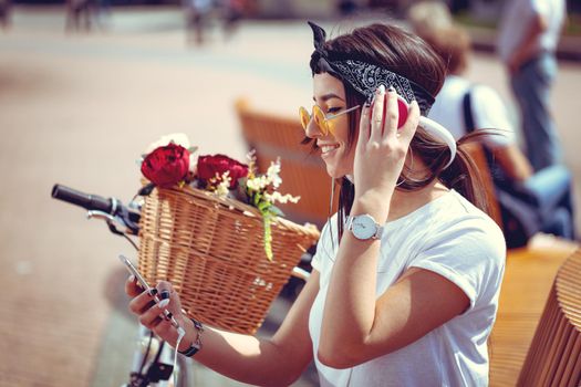 Attractive young woman is trying to find the melody she like best, during the stop of riding bike on the city street. She is glad of doing this. 