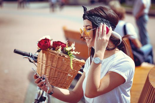 Attractive young woman is trying to find the melody she like best, during the stop of riding bike on the city street. She is glad of doing this. 