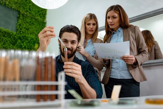 Team of a university biologists analysing the sample of plant in the lab tube, watering it with drops of nutritious fluid.