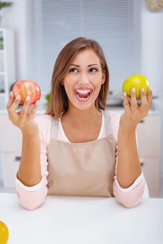Adorable young woman with cheerful expression, holds two fresh apples, demonstrates her breakfast,