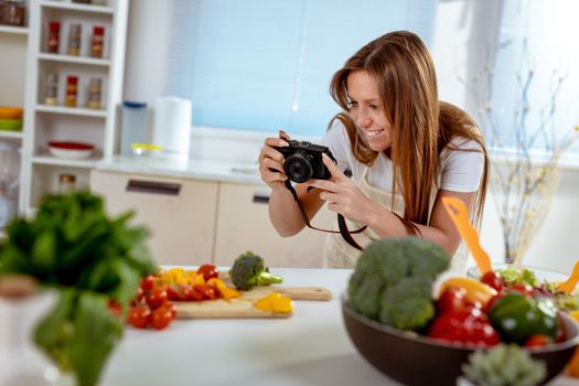 Beautiful young woman taking photo of healthy salad with digital photo camera for her blog.