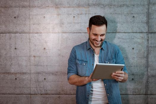 Young handsome successful entrepreneur looking on his tablet, checking plans before starting to work on construction site.