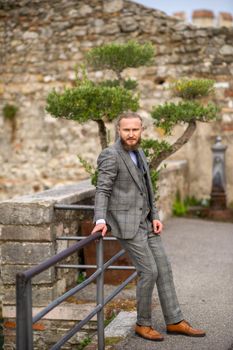 A man with a beard in a strict grey three-piece suit with a tie in the old town of Sirmione, a Stylish man in a grey suit in Italy.