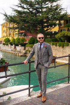 A man with a beard in a strict grey three-piece suit with a tie in the old town of Sirmione, a Stylish man in a grey suit in Italy.