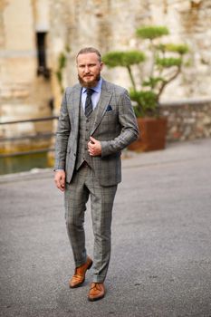 A man with a beard in a strict grey three-piece suit with a tie in the old town of Sirmione, a Stylish man in a grey suit in Italy.