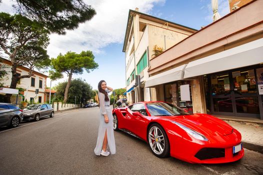 A girl in a dress next to a sports car on a city street in Tuscany.Italy.