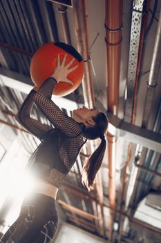 Young muscular woman doing exercise with wallball at the garage gym. She have a hard cross training.