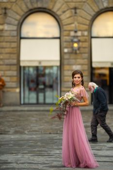 A bride in a pink dress with a bouquet stands in the center of the Old City of Florence in Italy.