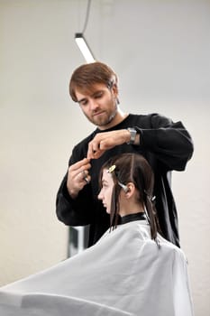 Professional male hairdresser with scissors cutting female hair in salon