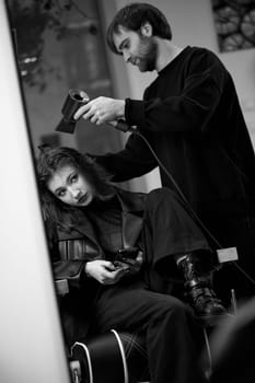 man hairdresser using hair dryer for female hair after washing in the beauty salon.