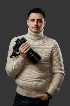 smiling professional handsome photographer in sweater with digital camera on gray background