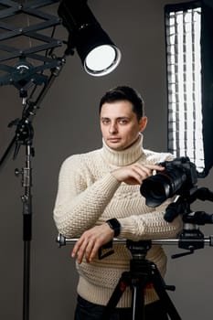 Professional handsome photographer with digital camera on tripod on gray background with lighting equipment