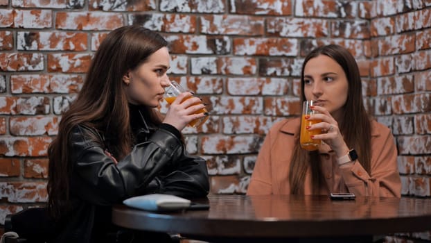 Two brown-haired girls talk in a cafe over glasses of juice